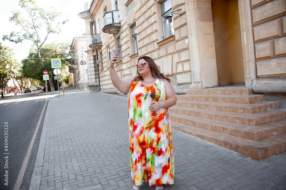 Beautiful fat woman dressed in summer dress  and glsses walking outdoor in the strreet of the city . Style overweight girl outdoor. Plus size concept