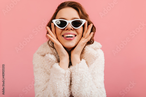 Cheerful young woman posing in sunglasses. Front view of laughing girl isolated on pink background.