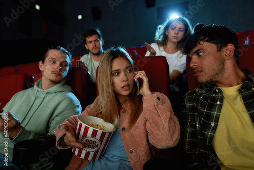Attractive young woman talking on the phone, annoying audience while watching movie with friends at the cinema