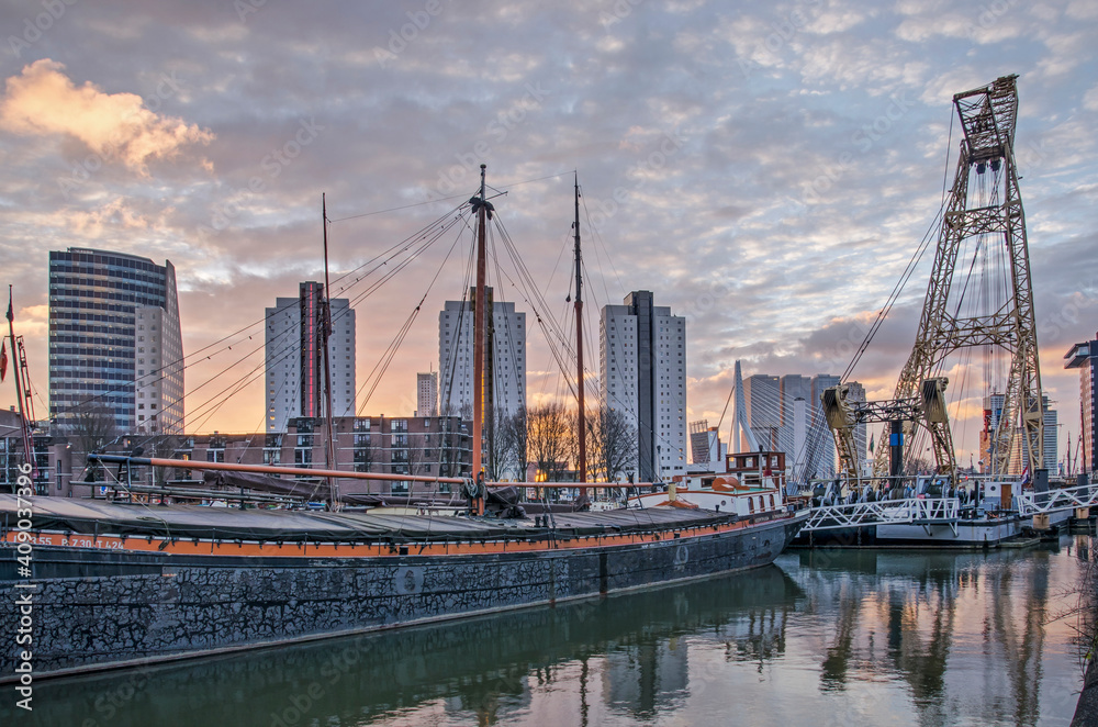 Fototapeta premium Rotterdam, The Netherlands, January 13, 2021: spectacular sky at sunrise over Leuvehaven harbour with historic barges and maritime equipment