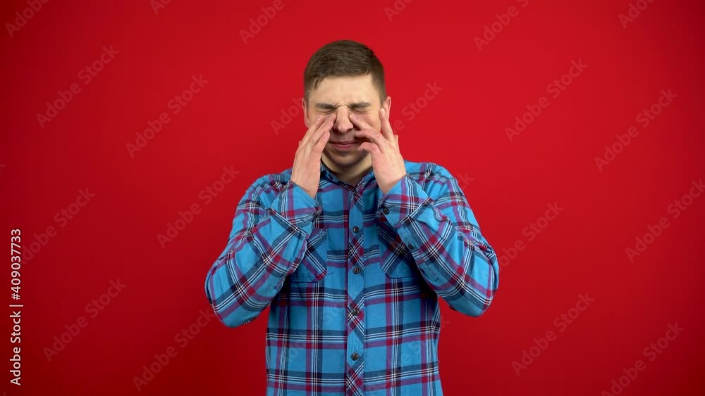 The young man has a sore nose, he touches it with his hand. Shooting on a red background. The young man has a sore nose, he touches it with his hand. Shooting on a red background.