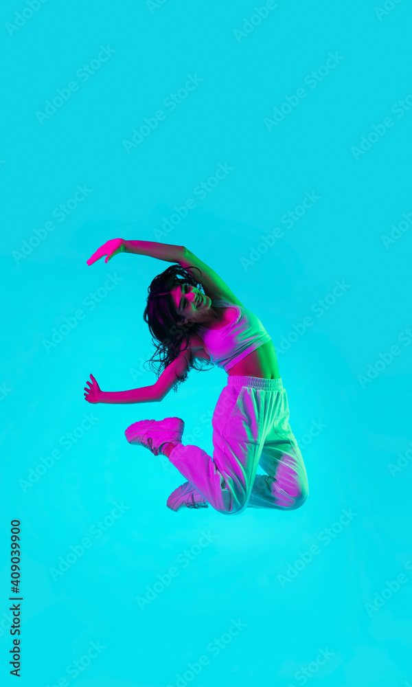 Overjoy. Brunette woman's portrait on blue studio background in mixed neon. Beautiful model jumping high, flying with hair blowed out. Concept of human emotions, facial expression, sales, ad, fashion.
