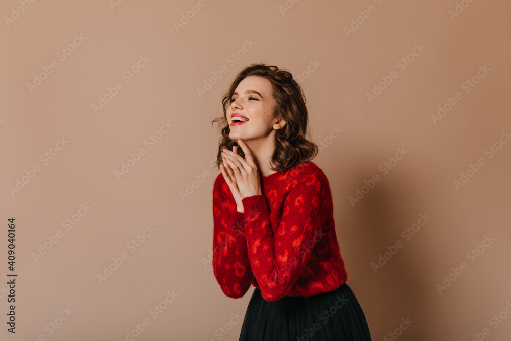 Excited girl in red sweater posing with folded hands. Studio shot of blithesome curly lady isolated on brown background. Excited girl in red sweater posing with folded hands. Studio shot of blithesome curly lady isolated on brown background.