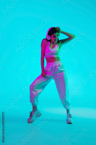 Fototapeta Naklejka Na Ścianę i Meble -  Art. Brunette woman's portrait on blue studio background in mixed neon. Beautiful model with headphones dancing inspired. Concept of human emotions, facial expression, sales, ad, fashion. Motion.