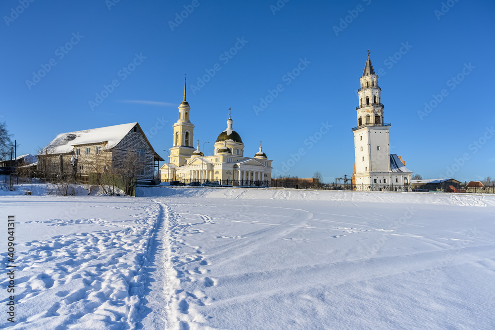 City landscape in the provincial town of Nevyansk (Russia) in a winter day. Frozen lake with a trodden path on white clean snow, leading to the church and the sloping madness 