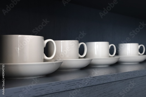 white porcelain teacups and saucers stand on a shelf with a wooden texture in blue-gray close-up