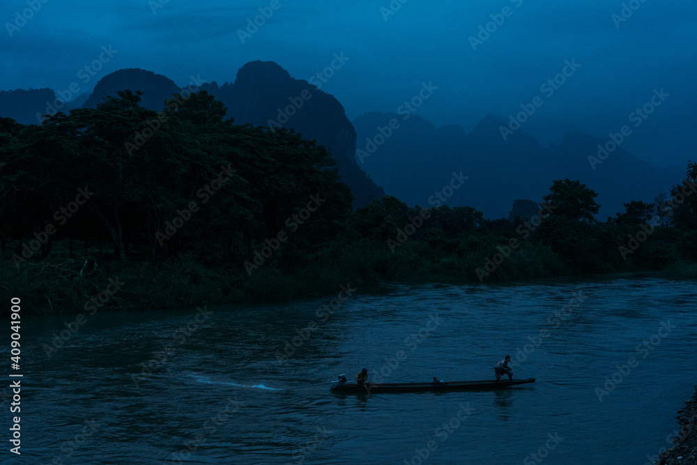 Small boat crossing river at dusk in Vang Vieng, Laos.