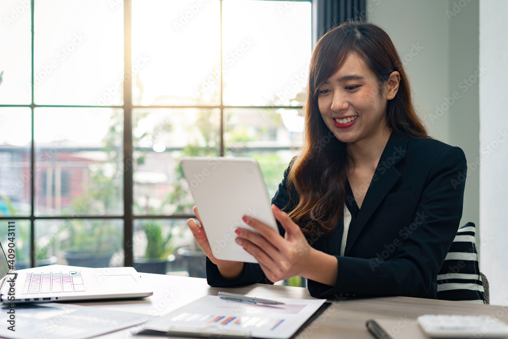 Asian female finance worker sitting at work, answering e-mails on the tablet. At home office table, sit at work with happiness and smile, work from home ideas. Asian female finance worker sitting at work, answering e-mails on the tablet. At home office table, sit at work with happiness and smile, work from home ideas.
