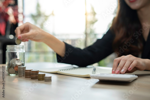 A close-up picture of a business woman putting a coin in a glass jar To save money and plan for it after retirement  money saving ideas And life after retirement