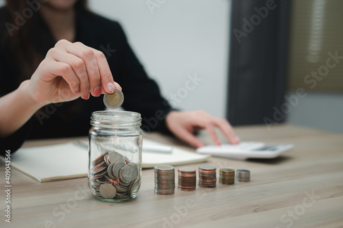 A close-up picture of a business woman putting a coin in a glass jar To save money and plan for it after retirement, money saving ideas And life after retirement