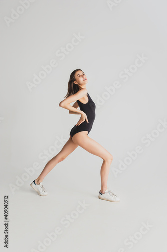 Stretching. Beautiful young woman's isolated on white studio background. Having fun, happy, full length. Dancing, getting crazy mood, stylish posing. Fit girl in black sportive swimsuit. Copyspace.