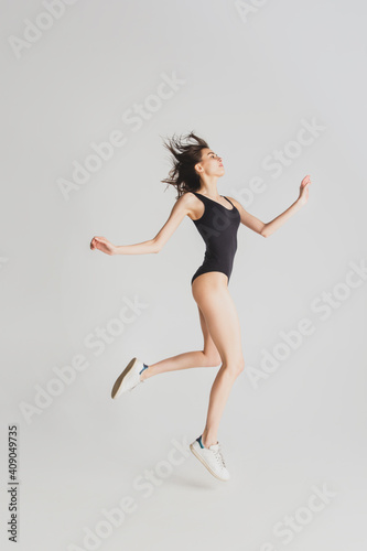 Fototapeta Naklejka Na Ścianę i Meble -  Jumping. Beautiful young woman's isolated on white studio background. Having fun, happy, full length. Dancing, getting crazy mood, stylish posing. Fit girl in black sportive swimsuit. Copyspace.