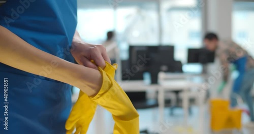 Close up of woman maid putting on rubber gloves with colleagues cleaning office on background