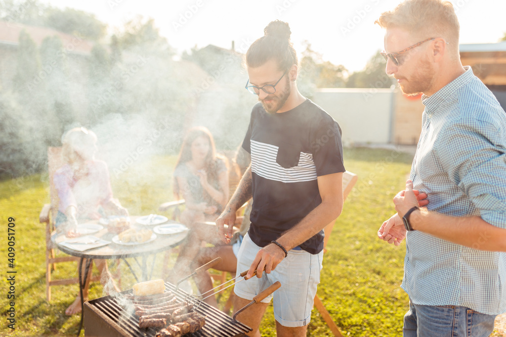 Obraz premium Men grilling meat while women are relaxing at backyard barbecue party