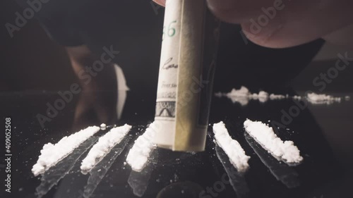 Cocaine junkie snorting line of coke with rolled US dollar bill. Drug Addiction.