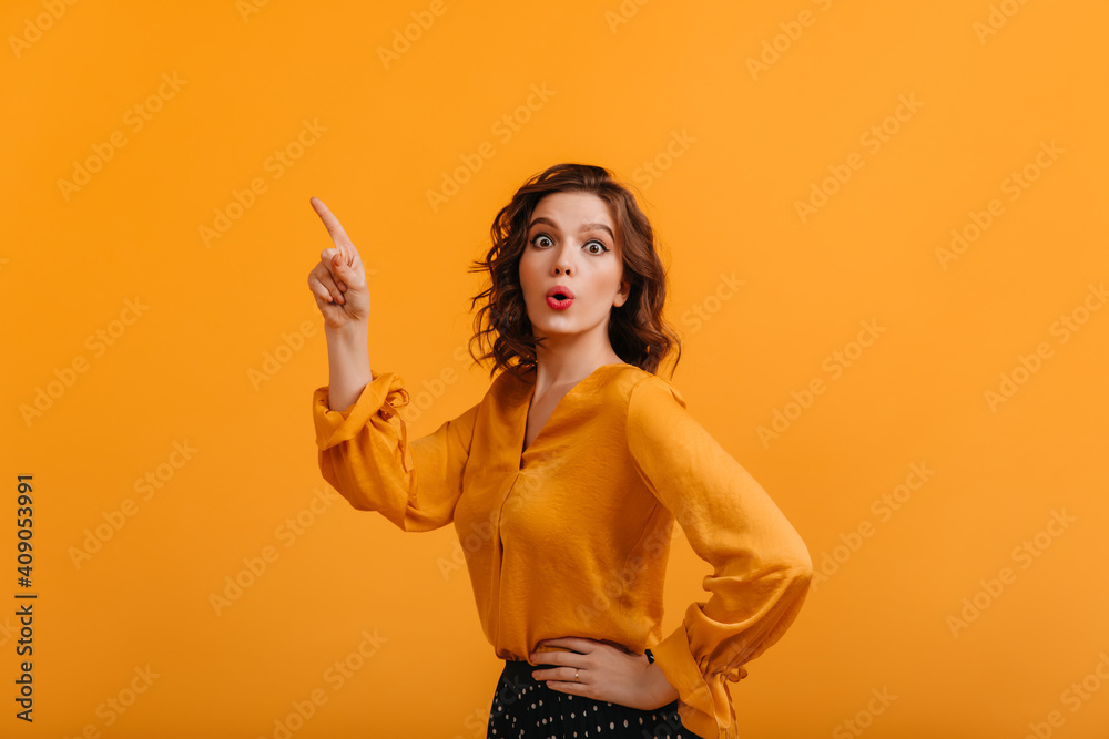 Shocked glamorous woman pointing with finger. Front view of amazed attractive girl isolated on yellow background. Shocked glamorous woman pointing with finger. Front view of amazed attractive girl isolated on yellow background.