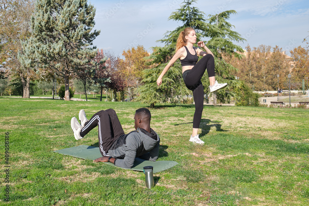 African black man and redhead caucasian woman exercising in a park with a mat. Fitness and sport outdoor. African black man and redhead caucasian woman exercising in a park with a mat. Fitness and sport outdoor.