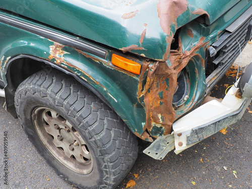 Fragment of a green car with a broken rusty front bent bumper and no headlight photo