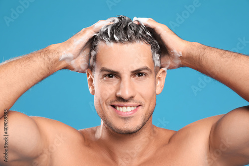 Handsome man washing hair on light blue background