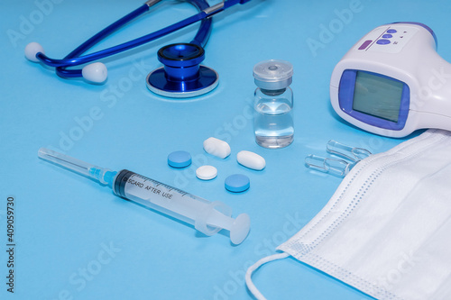 Ampoule, vial, syringe under white protective mask and non contact thermometer, stethoscope on blue background. Vaccination concept, disease prevention. Health care, Coronavirus vaccine development.