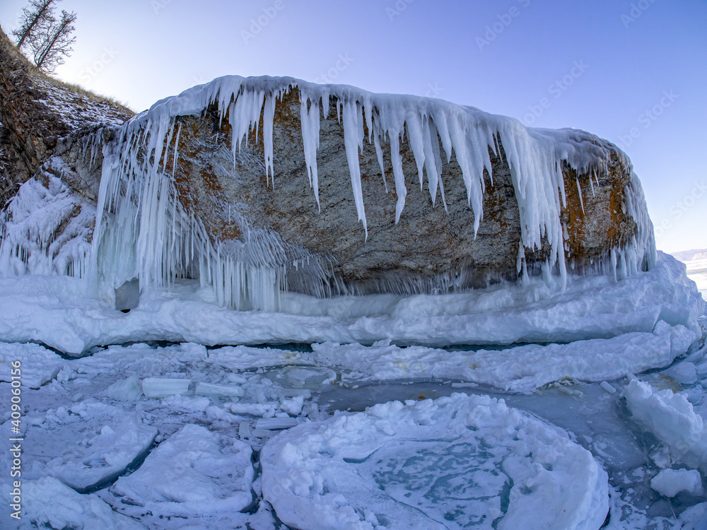 Long icicles hangs down under huge flat stone over frozen ice surface of  the Baikal lake near frozen stony shore with snow in Siberia, Russia.  Frozen winter landscape. Stock Photo | Adobe