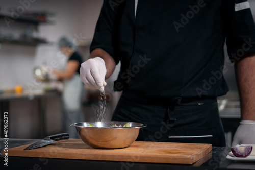 chef cook hands in gloves adding salt in greek salad at restaurant kitchen
