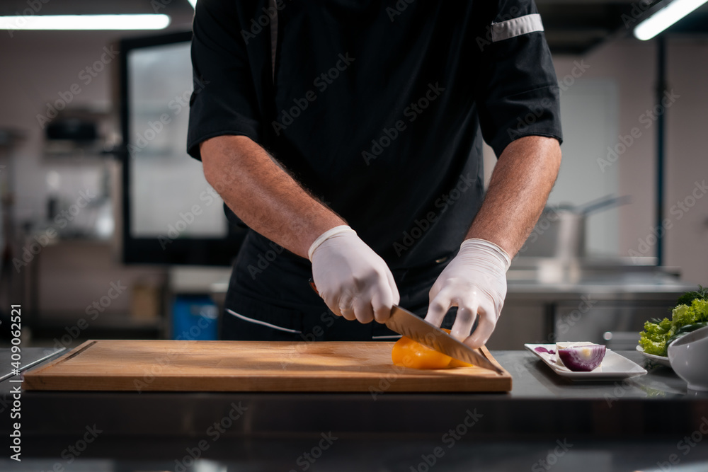 close up of chef cook hands in gloves cutting or chop yellow pepper at kitchen