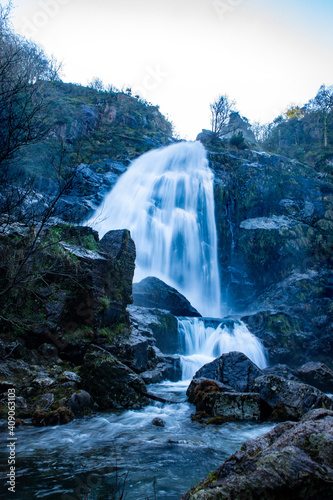 Cascada en medio del bosque rodeada de rocas y musgo verde durante el invierno