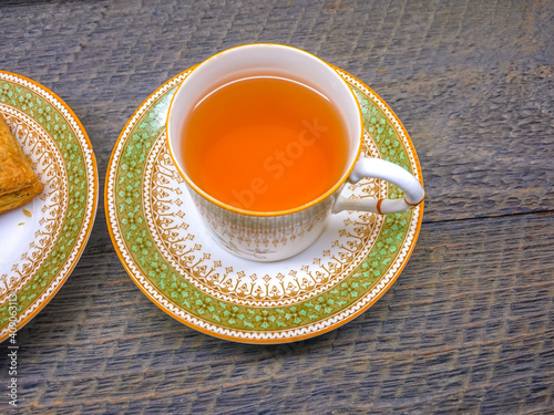 Hot tea in vintage picture of antique hot tea cup and bakery in saucer on wood background. Hot tea in vintage picture of antique hot tea cup and bakery in saucer on wood background