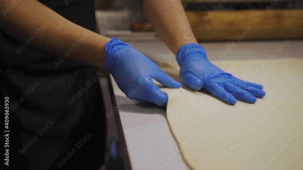 Baker With Gloves Stretching Dough For Cinnamon Roll. - close up Baker With Gloves Stretching Dough For Cinnamon Roll. - close up