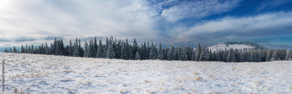 A snow-covered plateau set against a cloudy sky and a mountain range. Winter mountain landscape. Panorama from multiple shots.