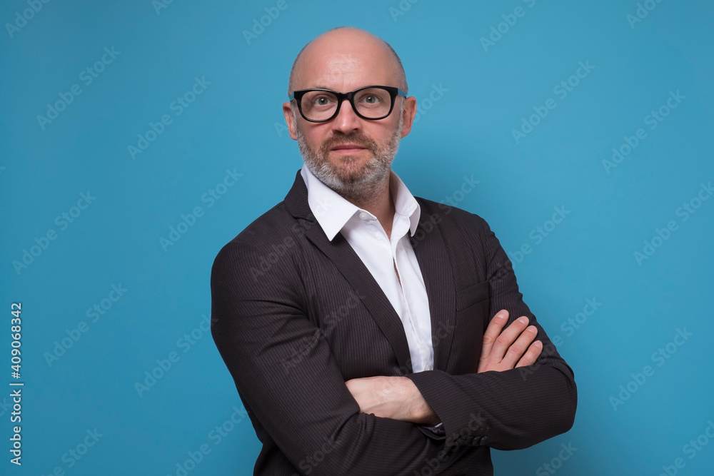 Handsome mature businessman in suit standing with arms crossed on blue background