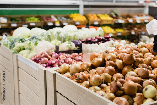 Fresh onions and vegetables on blurred background in supermarket