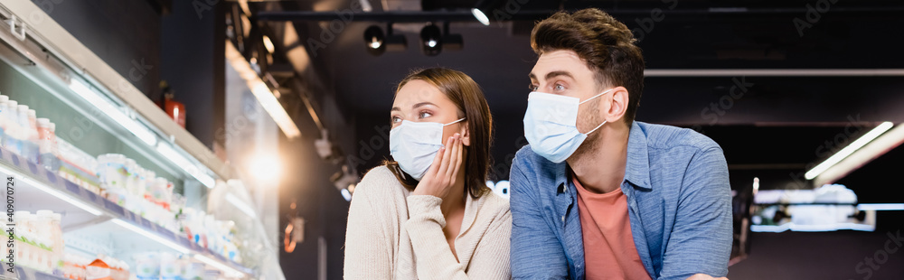 Young couple in medical masks in supermarket, banner