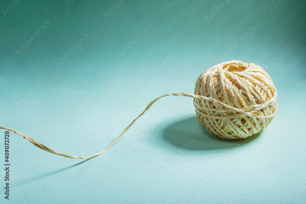 A skein of yellow twine with a loose thread on a light green background