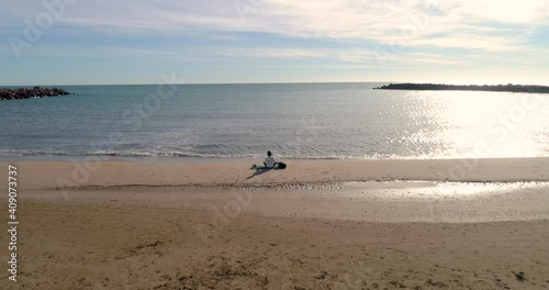 Mujer sola en la playa sentada haciendo yoga y un dron volando de espalda photo