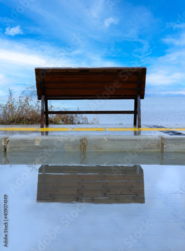 Empty bench reflection with blue and cloudy sky. Selective focus.