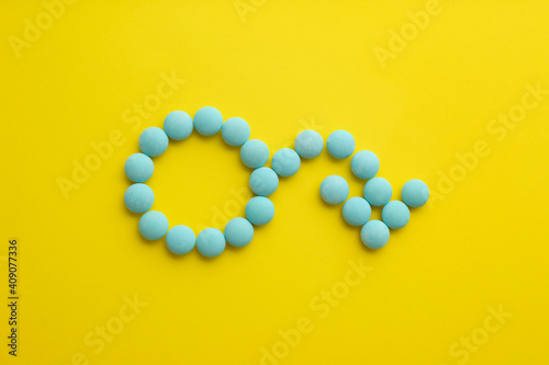 Male sign with bent arrow of blue pills symbolizing potency problems on yellow background, flat lay