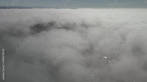 Drone footage above the clouds, showing expanse of white soft fluffy clouds, with mountains in the distance, USA below, scattered clouds with peaks to the ground. photo