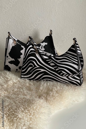 Woman’s cow and zebra printed little black and white bags lying on beige fur. Style and fashion. Accessories