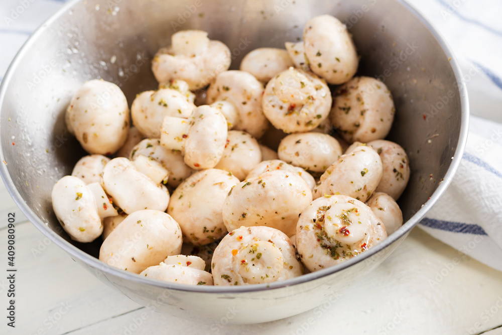Raw champignon mushrooms in a bowl on white rustic background prepared for baking. Raw champignon mushrooms in a bowl on white rustic background prepared for baking.