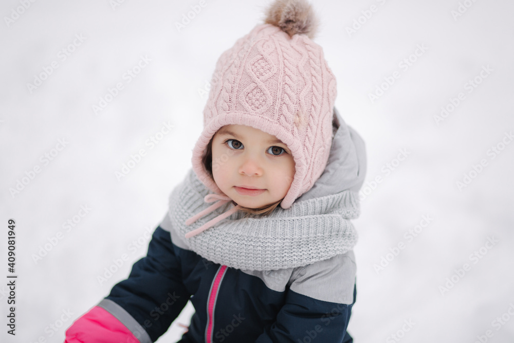 Happy little girl walking in the park on snow. Adorable little girl in a pink hat and overalls walking in the woods on a winter snowy day Happy little girl walking in the park on snow. Adorable little girl in a pink hat and overalls walking in the woods on a winter snowy day