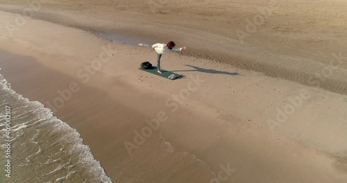 Mujer en la playa solitaria postura equilibrio de yoga y dron orbitando photo