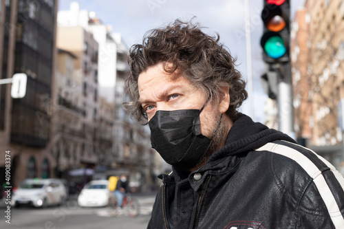 portrait of blue-eyed Caucasian man with black mask for prevention of contagion next to traffic light