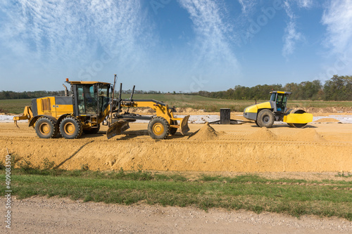 Preparation of the foundation for new highway. Tamping and leveling with a vibrating roller and grader