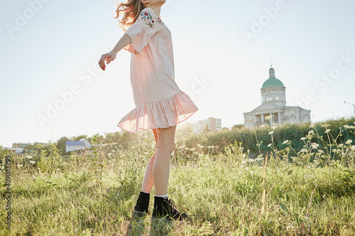 Blonde girl in pink linen dress spins in the field of flowers summer and sunlight