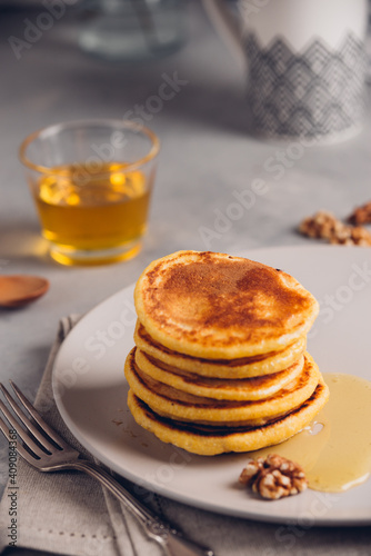 Yellow pancakes with corn flour and turmeric, dressed honey and red grapes. Healthy breakfast with superfoods. Light background, hugge scandinavian style
