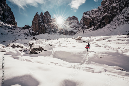 Two alpinists descending on snowy trail against sun rays in Dolomites photo