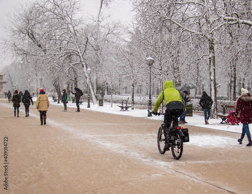 man with green jacket cycling with a sport bike in winter on a snowstorm on park with phone and camera