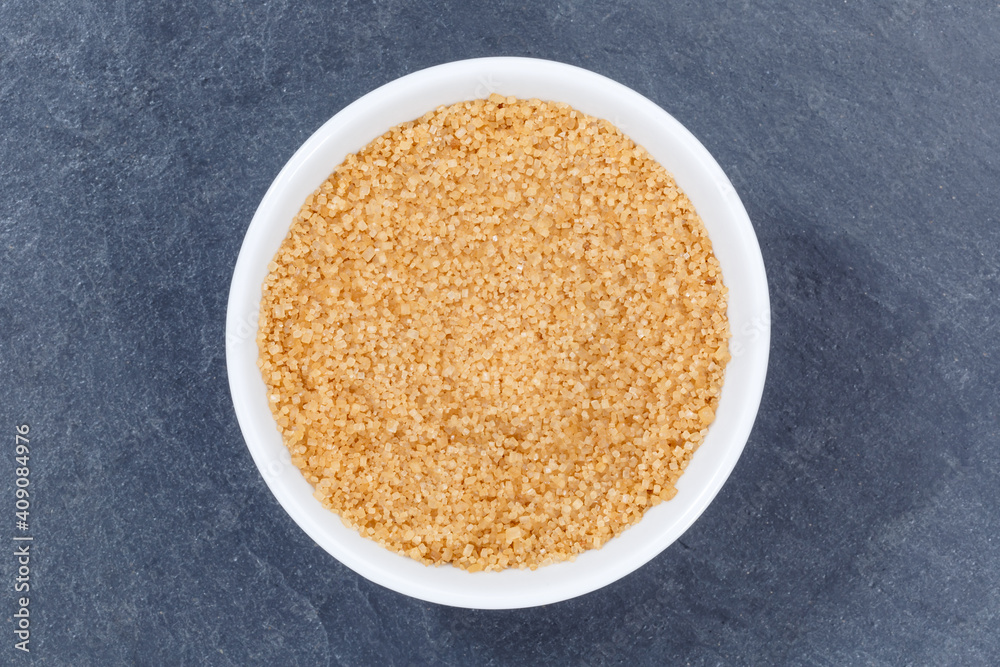 Brown cane sugar from above bowl on a slate Brown cane sugar from above bowl on a slate